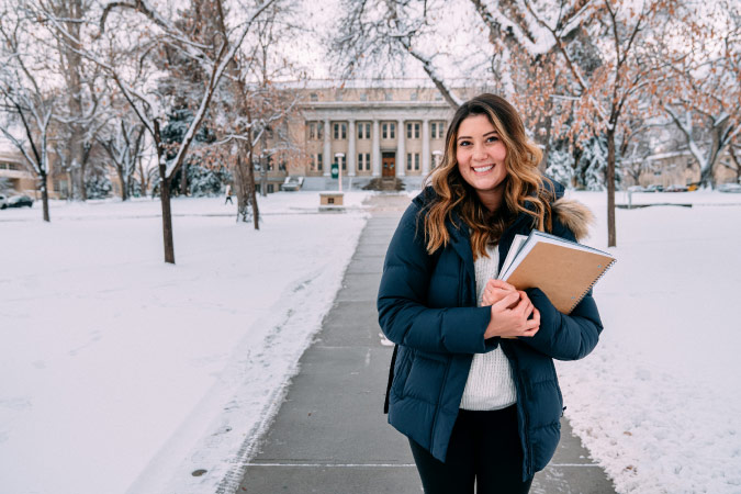 A happy student poses with her textbooks on the campus of Colorado State University in Fort Collins on a snowy day.