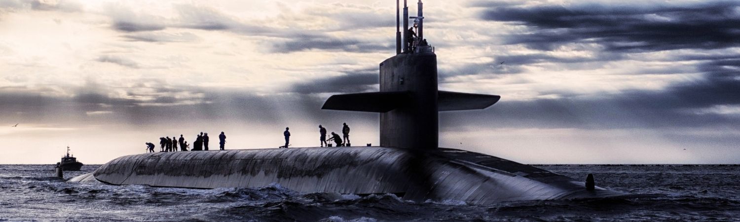 Submarine surfaced at sea with crew standing on the deck under a cloudy sky.