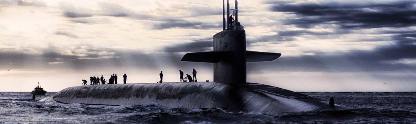 Submarine surfaced at sea with crew standing on the deck under a cloudy sky.