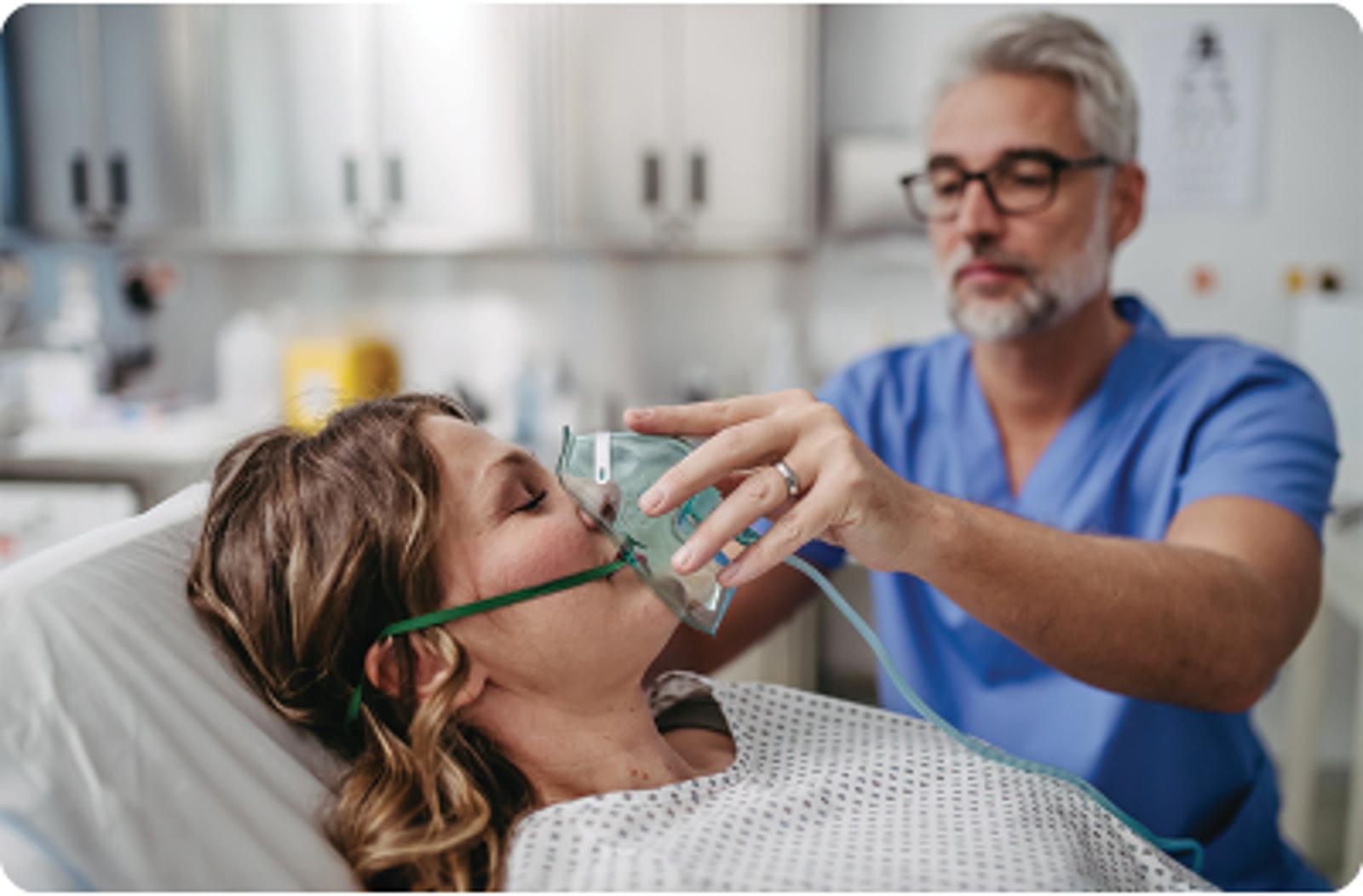 Healthcare professional administering oxygen through mask to patient in hospital bed during respiratory treatment