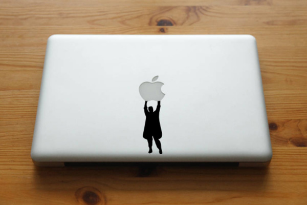 Sticker of a person holding onto an apple on MacBook.
