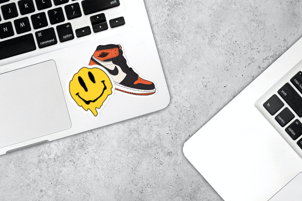 A sneaker and smiley sticker that needs to be removed from a laptop.