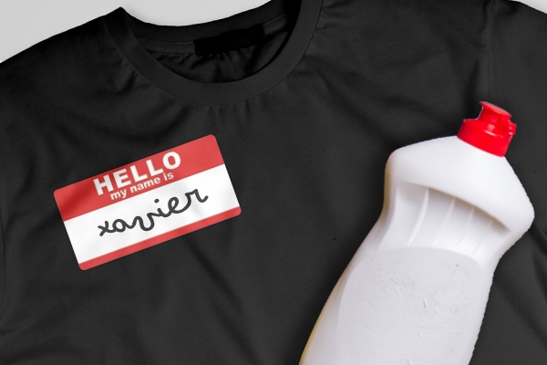 A bottle of dish soap left on top of a t-shirt that has a name sticker in the middle.