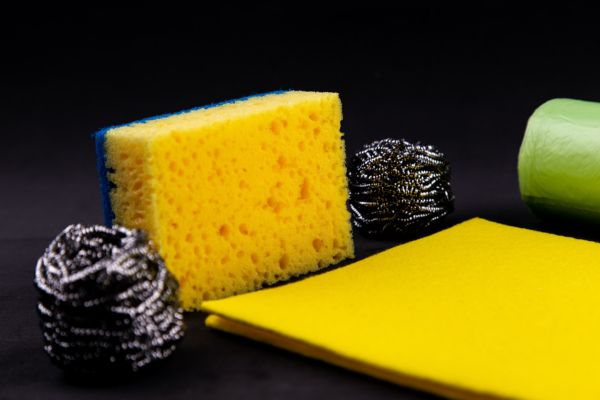 A yellow sponge, two black metal scrappers, and two yellow sponge cloths left on top of a black table