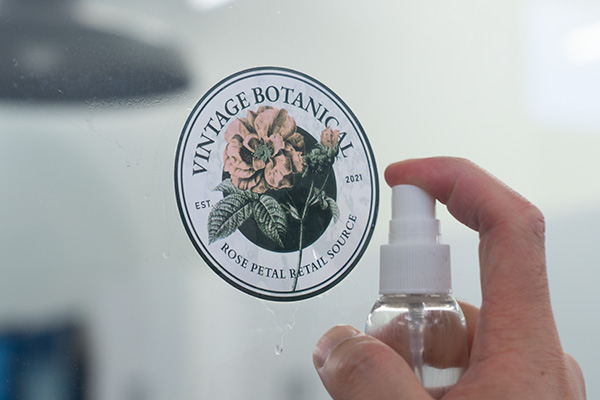 A person spraying an alcohol-based solution onto a sticker.