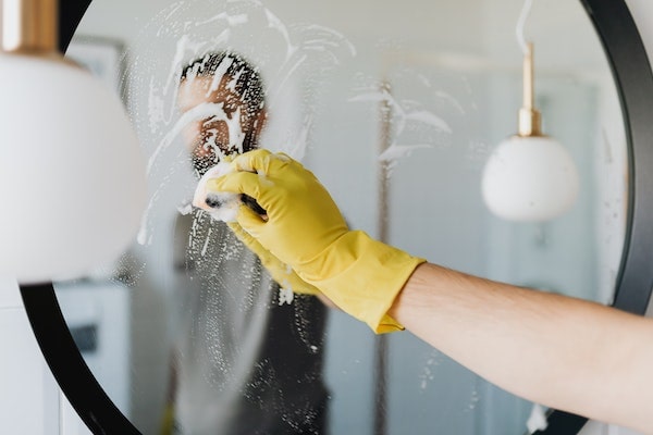 A person cleaning a round mirror with hot water and soap.