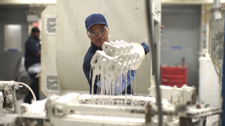 Employee dipping investment casting mold into slurry